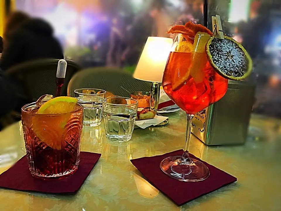 Aperitivo al tavolo da Ceraldi Caffè: calice con fetta d'agrume disidratata e un cocktail su tovaglioli bordeaux