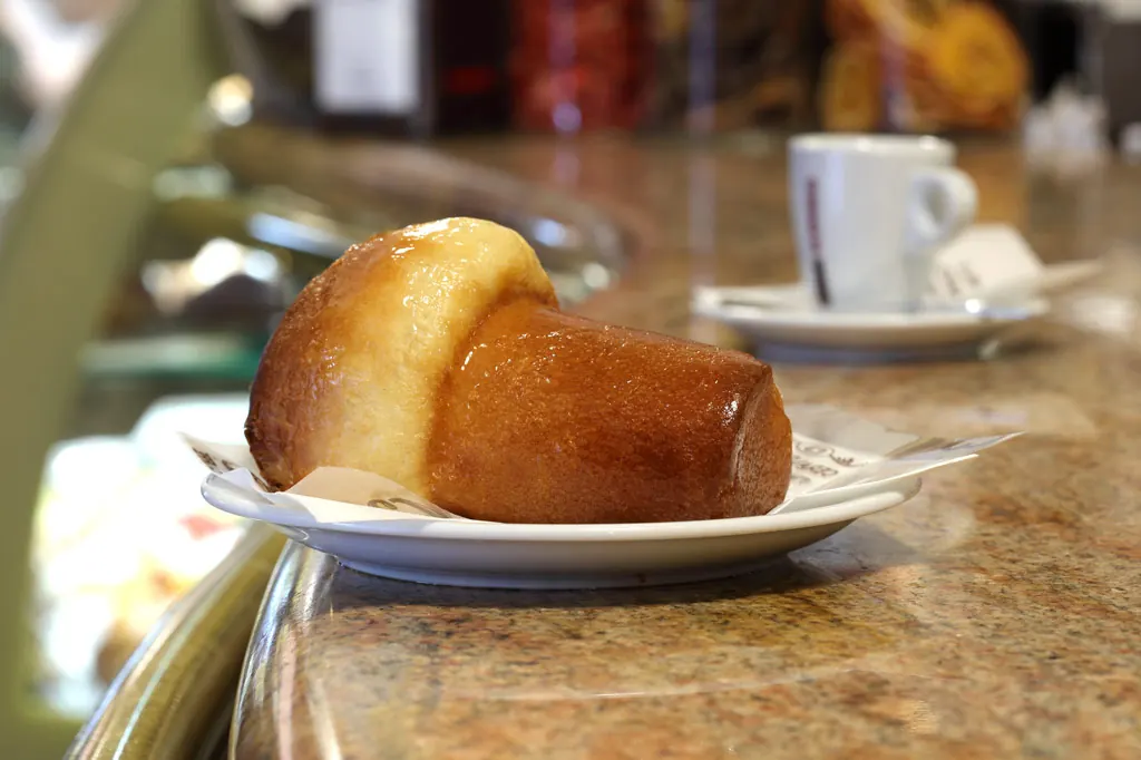 Babà al rum classico di Ceraldi Caffè, accanto a una tazzina di caffè